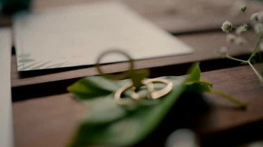 slow motion of two wedding rings that lie on green leaves on a wooden table and decorative rings fall on them