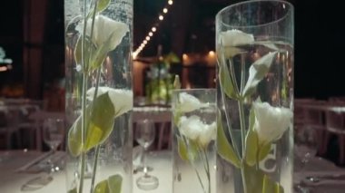 A glass vase with white flowers on the table in the event hall. Wedding table design