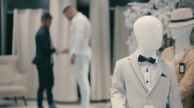 Damat düğün için şık bir erkek giyim mağazasında hazırlanır ve giyinir. Bir tezgahtar damadın giyinmesine yardım eder..