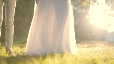 Gelin ve damat güneşli bir günde çayırda. Gelinliğiyle kıvrılan bir gelinin ağır çekimde