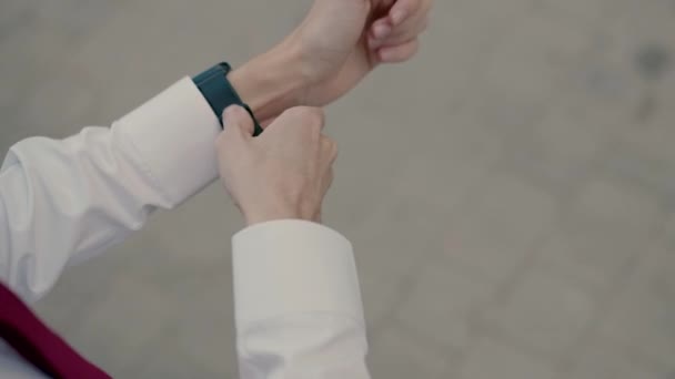 エレガントなシャツとバーガンディのネクタイの男は昼間外に立っている間に腕に腕時計ストラップを閉じます — ストック動画