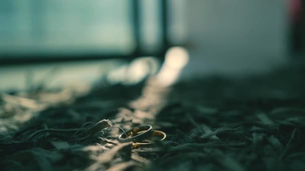 結婚指輪は太陽の光の下で灰色のカーペットの上にあり2つ目の指輪はそれの上に落ちる スローモーション — ストック動画