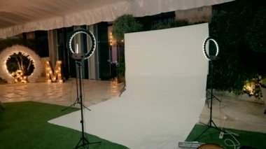 Konukların fotoğraflarını çekmek için etkinlik salonunun girişinde beyaz kağıttan yapılmış beyaz bir arka plan duruyor. Düğün fotoğrafları için beyaz arka plan. Fotoğraf için LED lambaları. Stüdyo.