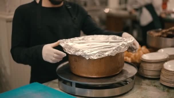 キッチンワーカーが中に肉を調理した鍋を開きます 蒸気が鍋から出てくる スローモーションで顔のないクローズアップビデオ撮影 — ストック動画