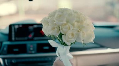 Bir buket beyaz gülü olan damat, gelini düğünlerine arabayla götürür. Araba sürerken arabanın içinde bir buket beyaz çiçeğin yakın çekim videosu.