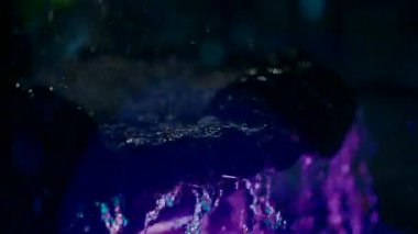 Close-up slow motion video recording of water falling in a fountain under purple LED lighting