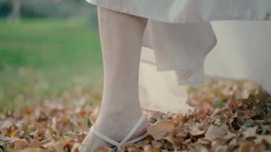 Close up slow motion video shoot of a brides feet walking on the yellow leaves that have fallen from the trees in autumn