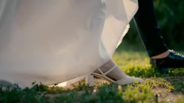 Close up slow motion shot of feet of bride and groom walking in the park on the grass