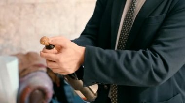 a man in a formal suit opens a bottle of champagne