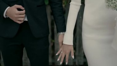 A bride and groom stand by a fence and hold each others hands. Beautiful slow motion video shoot of a bride and groom on a wedding day. Hand in hand next to each other.