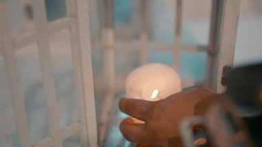 Close up video shot of a man lighting a candle and putting it in a white vintage style lamp at evening.