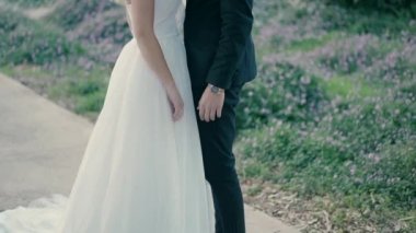 A bride and groom are standing in a beautiful park on the path, facing each other and holding hands.