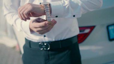 A man wearing an elegant white shirt closes the gold watch on his arm. Close-up visado slow motion shot.