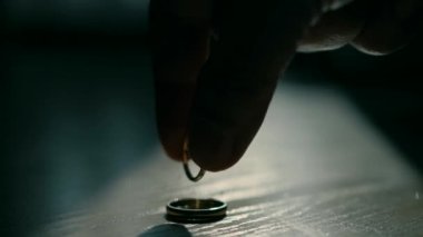 Close-up of wedding rings. A man spins one ring inside another ring in the dark on the wooden table.