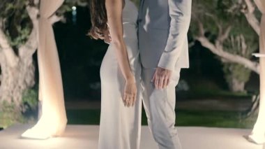 Bir damat ve bir gelin, düğün günü gölgeliğin yanında karşı karşıya durur ve el ele tutuşurlar..