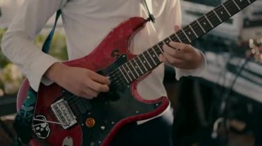 Close-up video shot of a boy in a white shirt playing a red guitar.