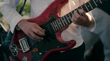 Close-up video shot of a boy in a white shirt playing a red guitar.