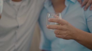 Beyaz tişörtlü ve gözlüklü iki adamın yakın çekim videosu. Bir kadeh şarap ve bir bardak viskiyle şerefe..