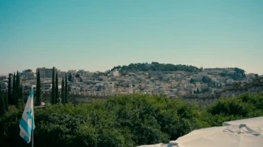 A beautiful view of Jerusalem with the Israeli flag in the foreground during the day.