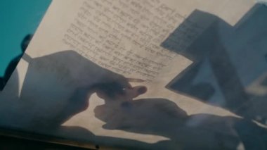 Beautiful video shot from below of writing a Torah scroll on the transparent glass table outside with a blue sky in the background. Shadow of a hand writing a Torah book. Judaism. Israel. Jerusalem.