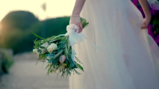 彼女の手に花束を持つ花嫁は 日没の遊歩道に沿って歩きます スローモーション — ストック動画