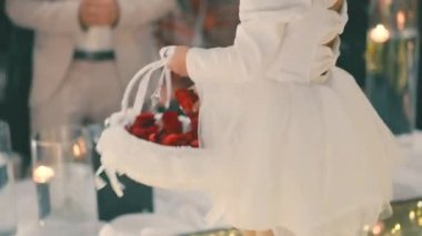 Beyaz elbiseli küçük bir kız beyaz bir sepetten kırmızı gül yaprakları fırlatıyor. düğün geleneği