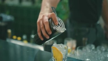 Bir barmen bardağa buz ve portakallı kokteyl doldurur..