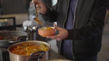 Yemek masasındaki büyük bir tencereden kuskus çorbası bir tabağa konur. Büyük kaşıklı bir adam çay tabağına çorba koyar..