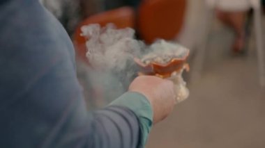 Bir insan yürür ve elinde dumanlı bir nesne tutar, Doğu ya da ruhani bir törenin bir parçası olarak..