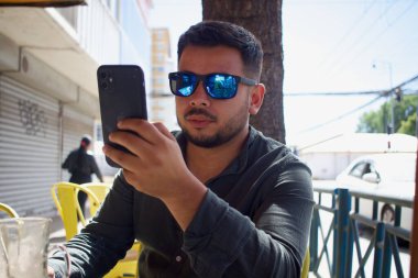 Şehir dışındaki bir kafede cep telefonuna bakan Latin bir adam.