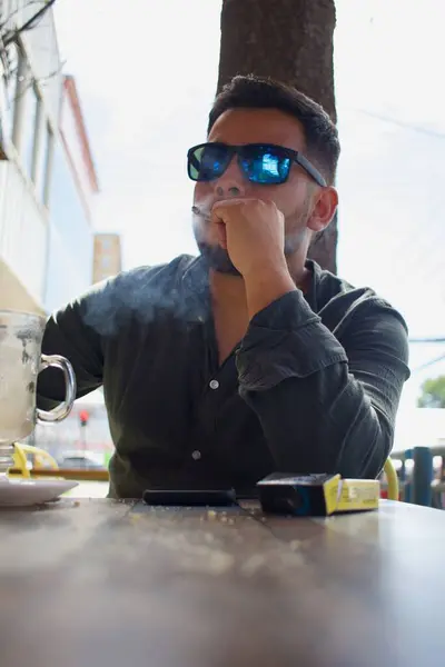 Latino person smoking a cigarette in an outdoor city coffee shop