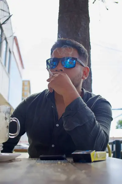 Latino person smoking a cigarette in an outdoor city coffee shopv