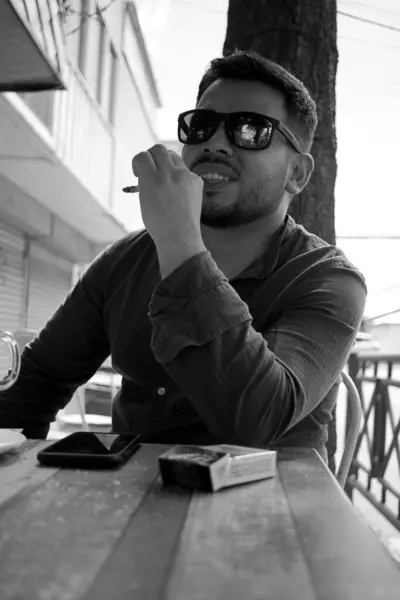 Latino person smoking a cigarette in an outdoor city coffee shop, black and white photography