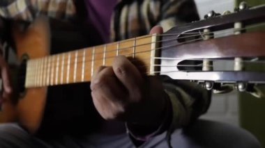 Adam oturmuş gitar çalışıyor.