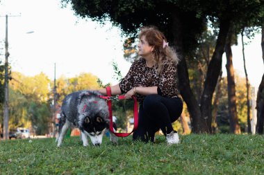 Latin bir kadın köpeğiyle parkta yürüyor.