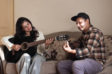 Latin bir baba ve kızı kanepede gitar çalıyor.