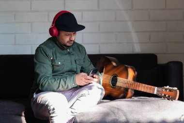 Kulaklıklı bir adam gitarın yanında cep telefonunu kontrol ediyor.