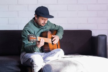 Solak adam kanepede oturup gitar çalıyor.