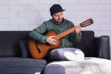 Şapkalı Latin adam evde gitar çalıyor.