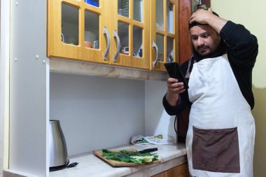 Adam yemek pişirirken telefonunu kontrol ediyor.