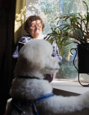 Yaşlı bir kadın köpeğiyle kitap okuyor.