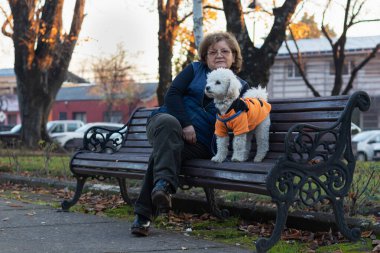 Yaşlı bir kadın ve köpeği bir sonbahar öğleden sonrasında parkta oturuyorlar.