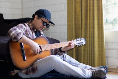 Latin bir adam yerde oturmuş gitar çalıyor.