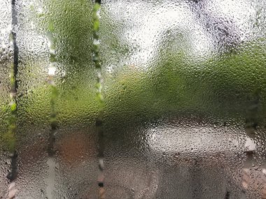 Buhar buharlaştırma suyu damlaları yağmurun önplanından sonra teras bahçesinin arka planında bulanık bir pencere. Seçici odak.