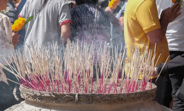 Religion photography of incense sticks burning on big joss stick pot with crowd Buddhist people background.