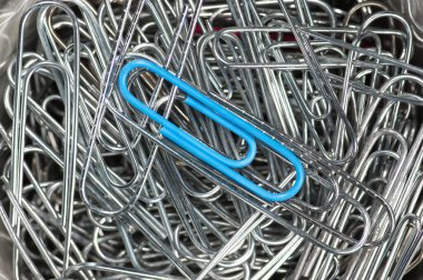 Single Blue paper clip in a pile of chrome ones clipart