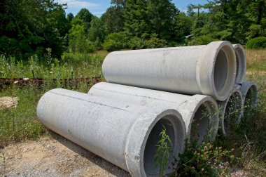 Çimenli bir alana yığılmış altı beton boru bölümü.