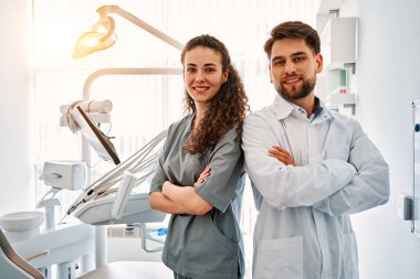 Diş muayenehanesindeki bir grup doktor sırt sırta verip kameraya bakıyor ve gülümsüyor. Doktorların işi ve boş vakitleri. Arka planda, dişçi koltuğu ve ekipman var. Uzayı kopyala. Güneş ışığı.                               