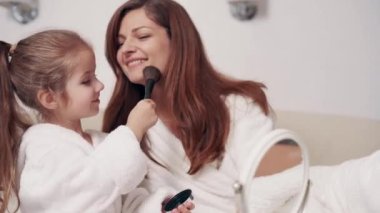 Sevimli anaokulu kızı makyaj yapmayı annesinden öğreniyor. Çocuk aynada kendine bakıyor..