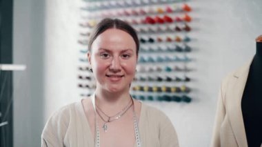 Genç, gülümseyen kadın terzi atölyede duruyor ve kameraya bakıyor. Sabit çekim.